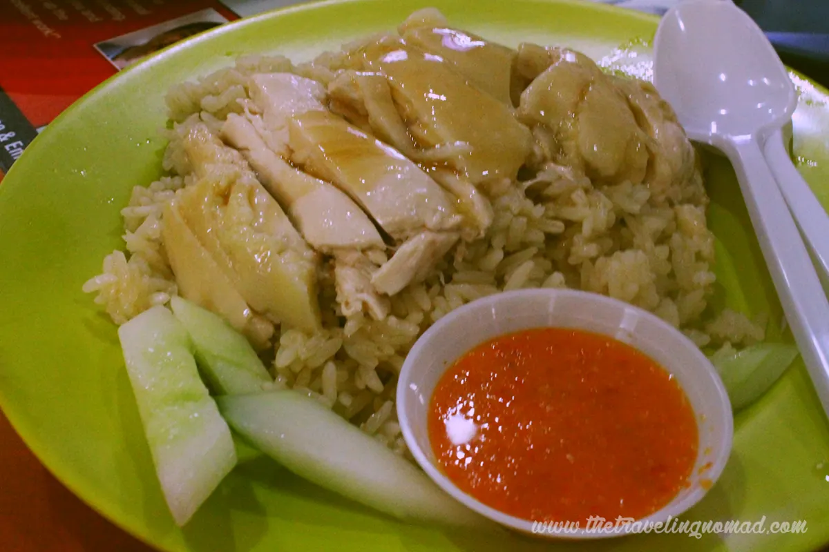 Hainanese chicken rice with sliced poached chicken, rice, cucumber and chilli sauce