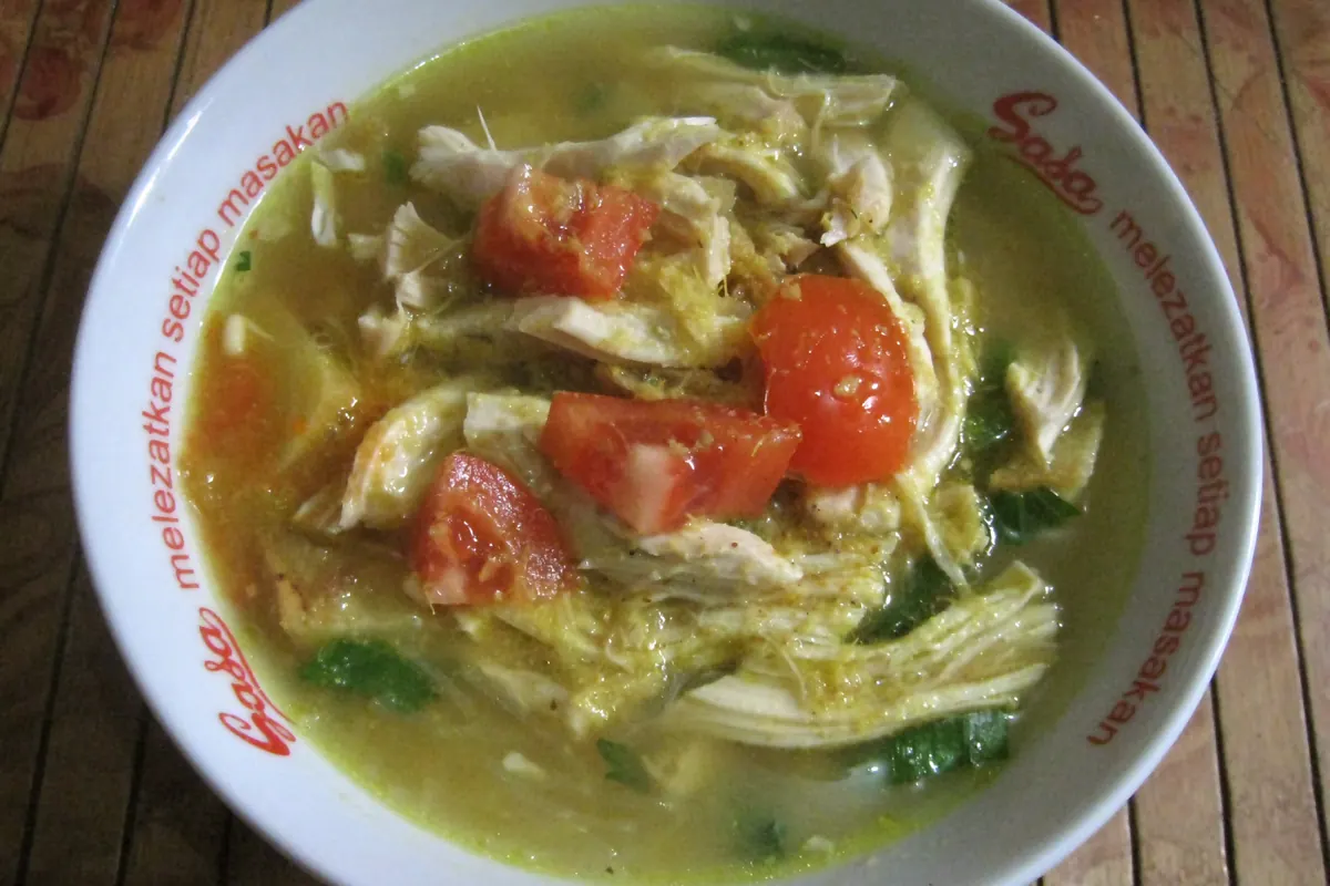 Bowl of soto ayam with shredded chicken, tomatoes and turmeric broth